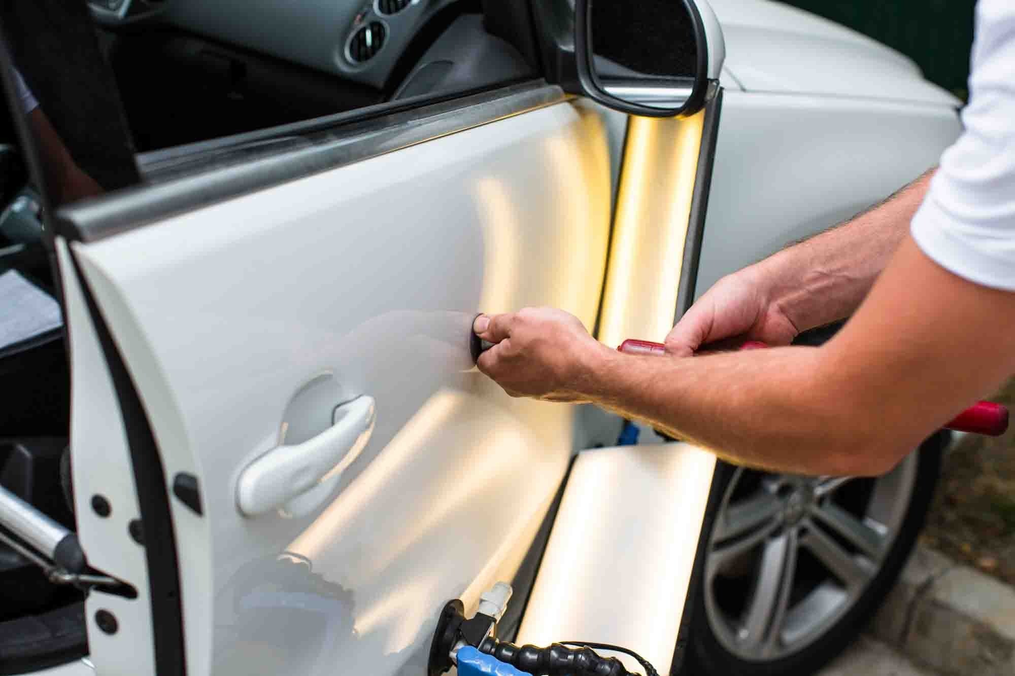 Technician performing paintless dent repair on white sedan