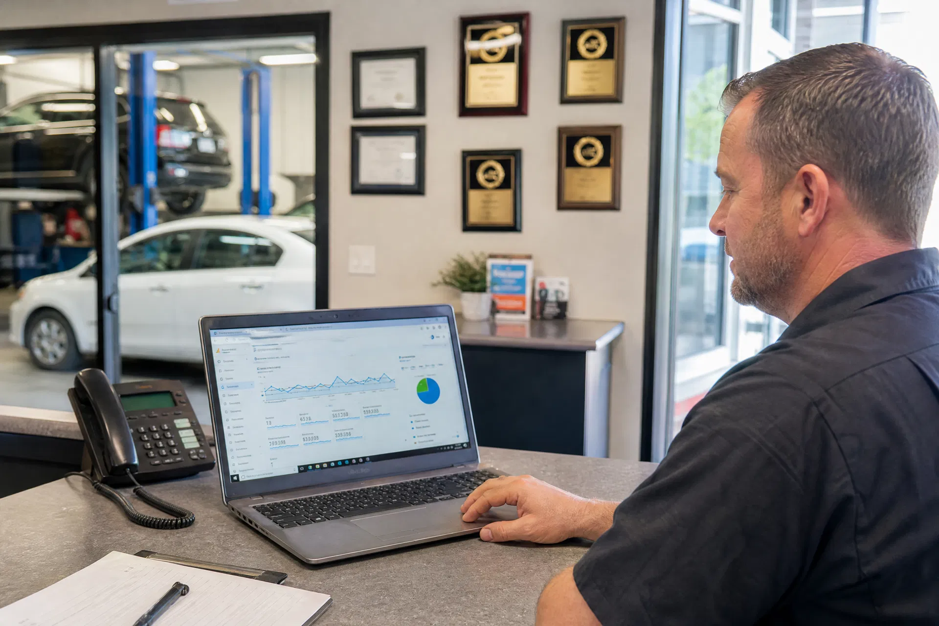 An auto shop owner reviewing Google Analytics at the reception desk, showing a significant upward trend in organic traffic and phone call conversions