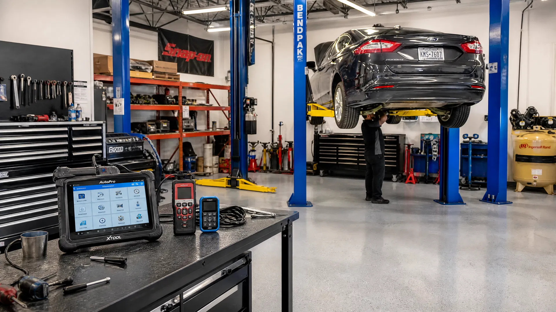 Inside a well-equipped auto repair shop with hydraulic lifts, OBD-II diagnostic scan tools, and a mechanic working on a vehicle — the essential equipment for opening an auto repair shop